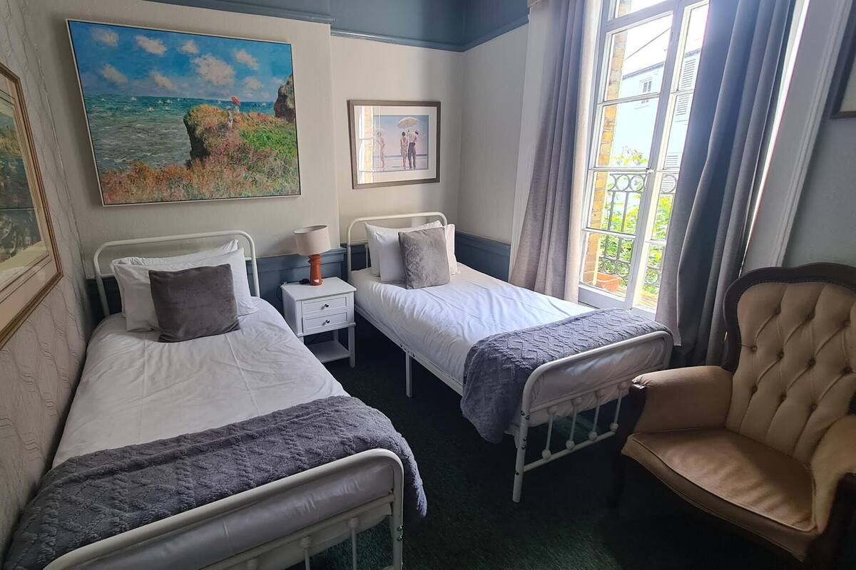 A room with two single beds, a chair, a nightstand with a lamp, and two framed pictures on the wall.