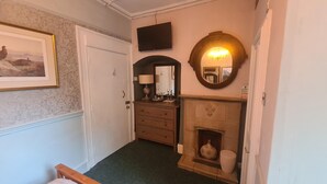 A hallway with a door, a framed picture, a television, a mirror, a fireplace, and a lamp. - Kings Boutique Hotel (London)