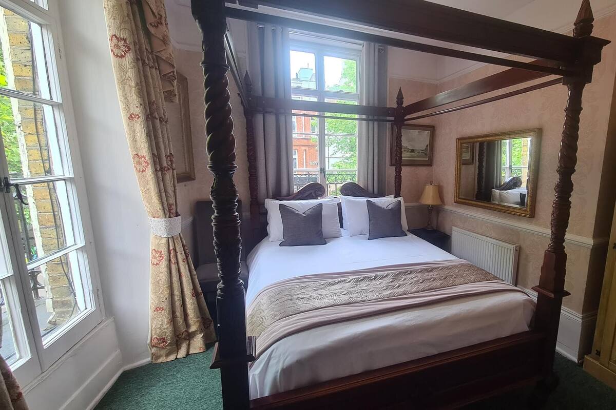 A four-poster bed with a canopy, a mirror, and a radiator in a room with a green carpet.
