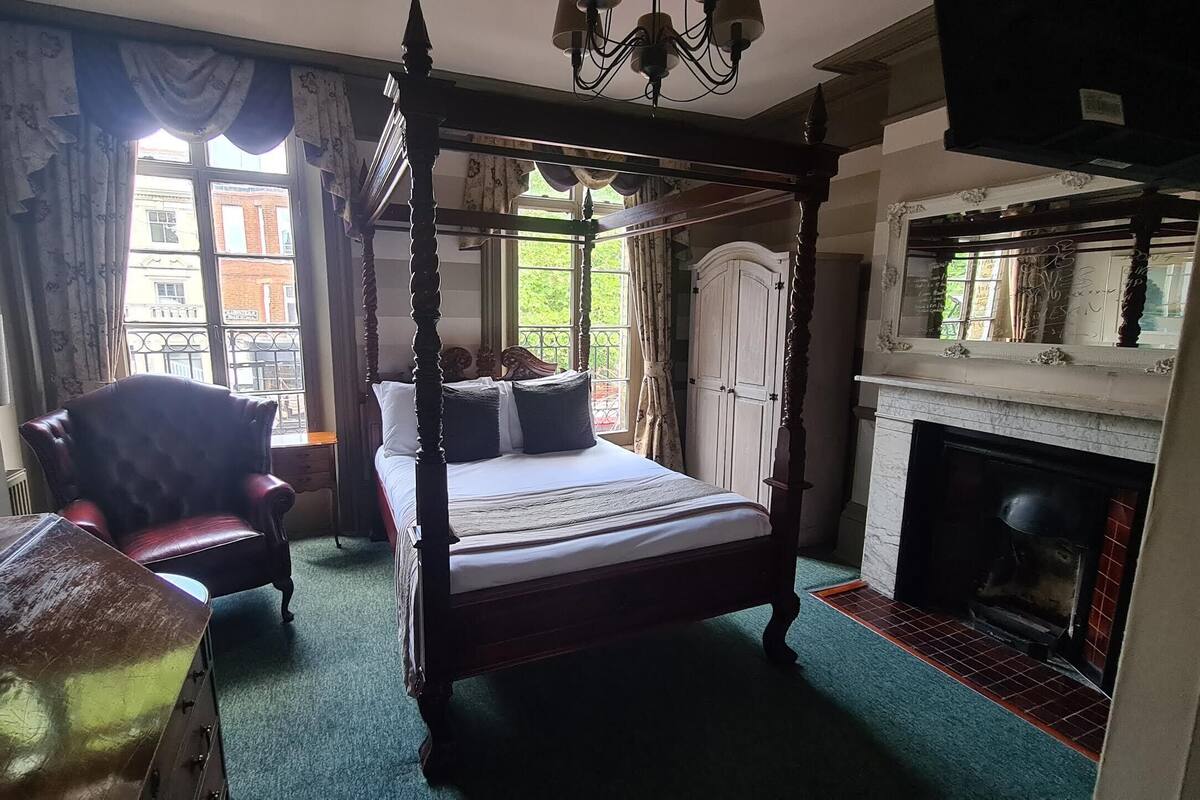 A four-poster bed with a canopy, a fireplace, and a view of the outside through large windows.
