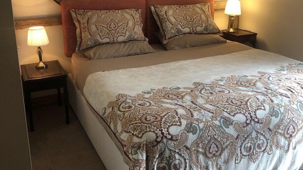 Een slaapkamer met een groot bed, twee nachtkastjes en een zichtbare houten balkenstructuur aan het plafond.