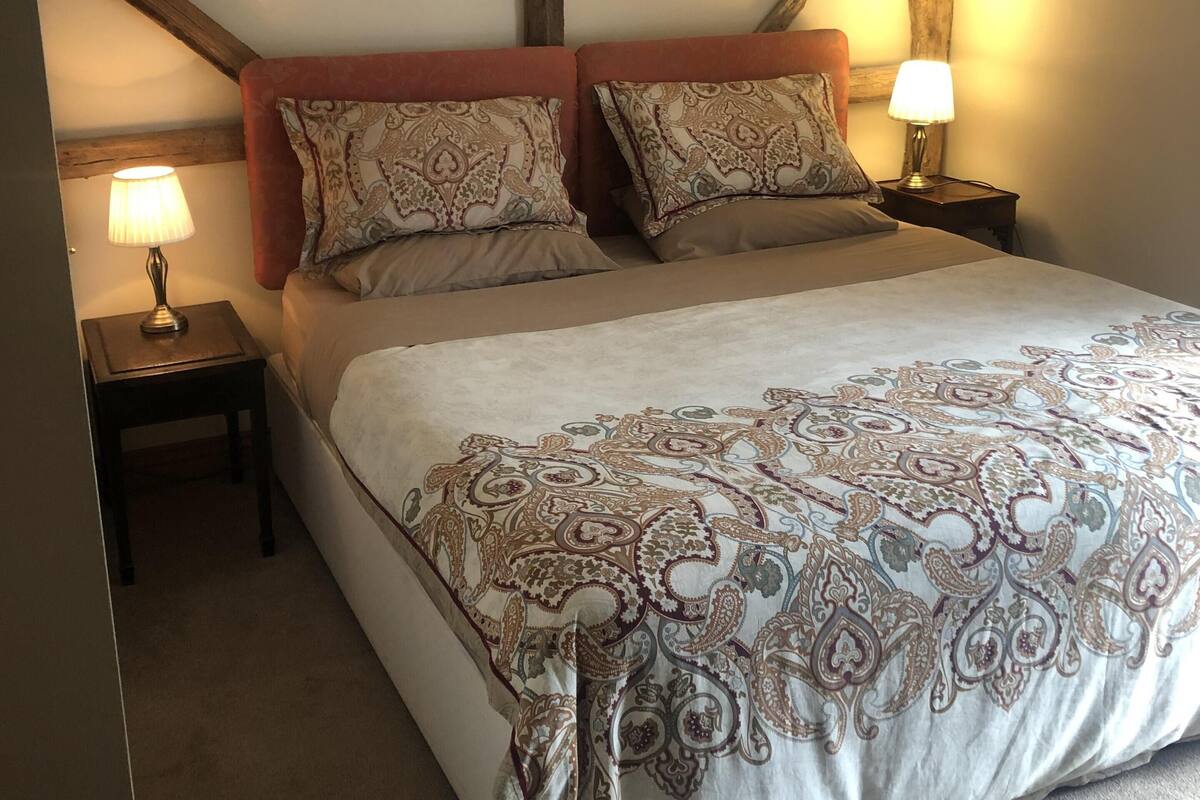 Une chambre avec un grand lit, deux tables de chevet et une structure de poutres apparentes en bois au plafond.