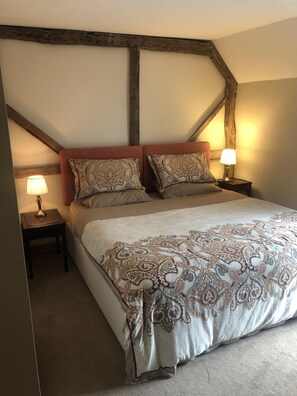 Une chambre avec un grand lit, deux tables de chevet et une structure de poutres apparentes en bois au plafond.