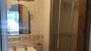 Een badkamer met een douche in een glazen cabine, een wastafel met spiegel erboven en een betegelde vloer.