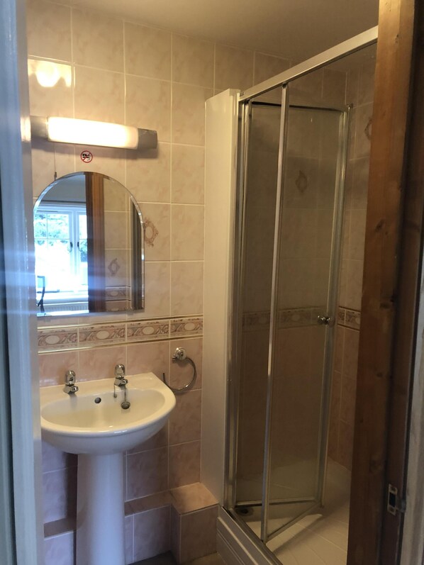 A bathroom with a glass-enclosed shower, a sink with a mirror above it, and a tiled floor. - Sir Alfred Munnings Hotel (Harleston)