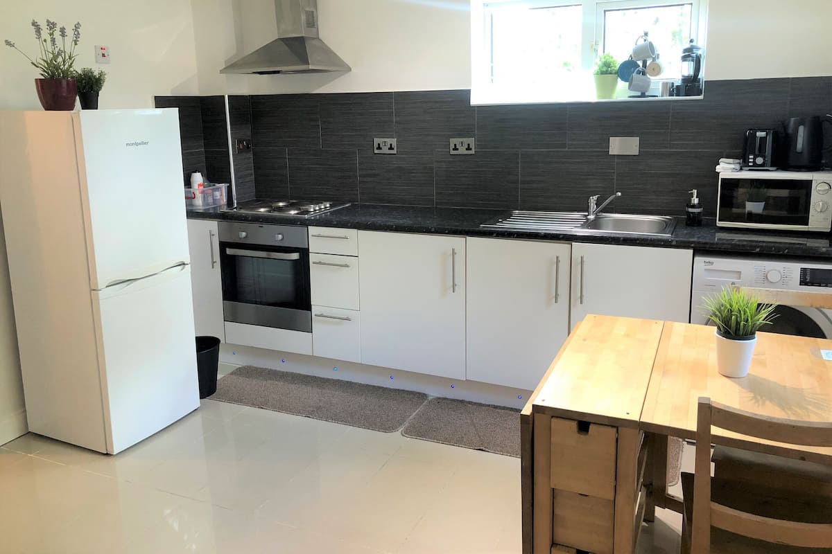 Una cocina moderna con armarios blancos, una estufa de acero inoxidable, horno empotrado, microondas y ventana sobre el lavadero.