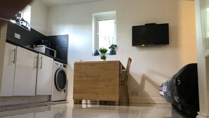Eine kompakte Küche mit Waschmaschine, einem Holztisch und einem an der Wand montierten Fernseher.