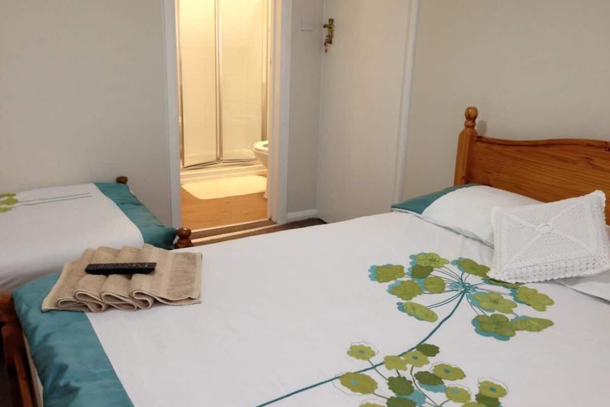 Habitación de hotel con dos camas, cabecera de madera, pared blanca y puerta que da a un baño.