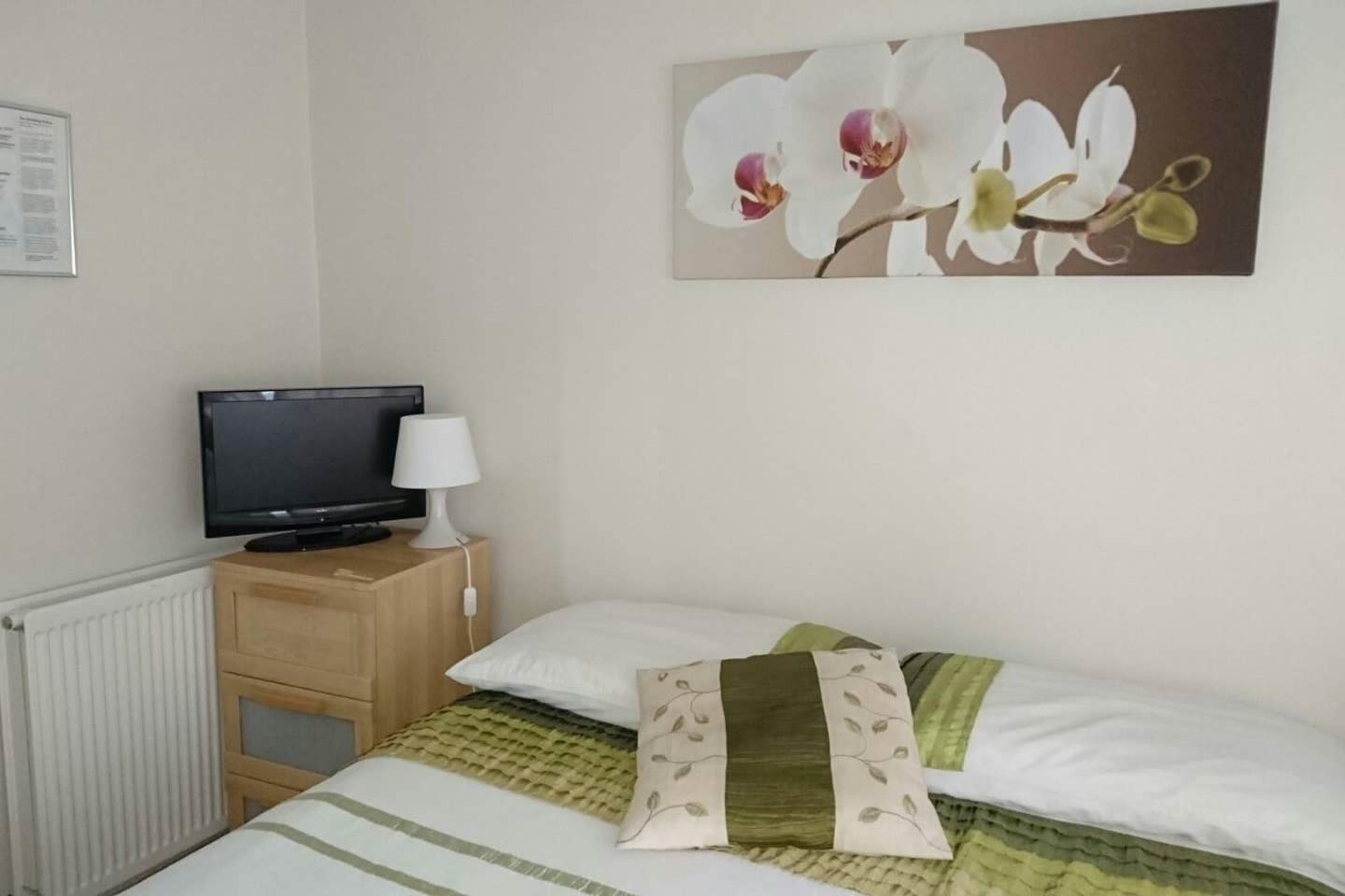 A bedroom with a bed, a television, a lamp, and a wall-mounted picture of orchids.