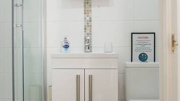 A bathroom with a glass shower enclosure, a white sink with a mirror above, and a toilet with a caution sign.