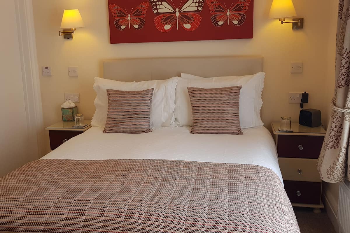 A neatly made bed with a patterned bedspread, two pillows, and a wall-mounted lamp.