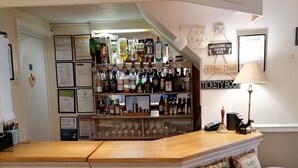 Una zona de bar con mostrador de madera, taburetes y diferentes botellas y vasos.