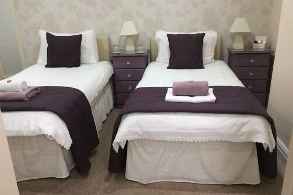 Two twin beds with white and dark-colored bedding, each with a bedside table and lamp.