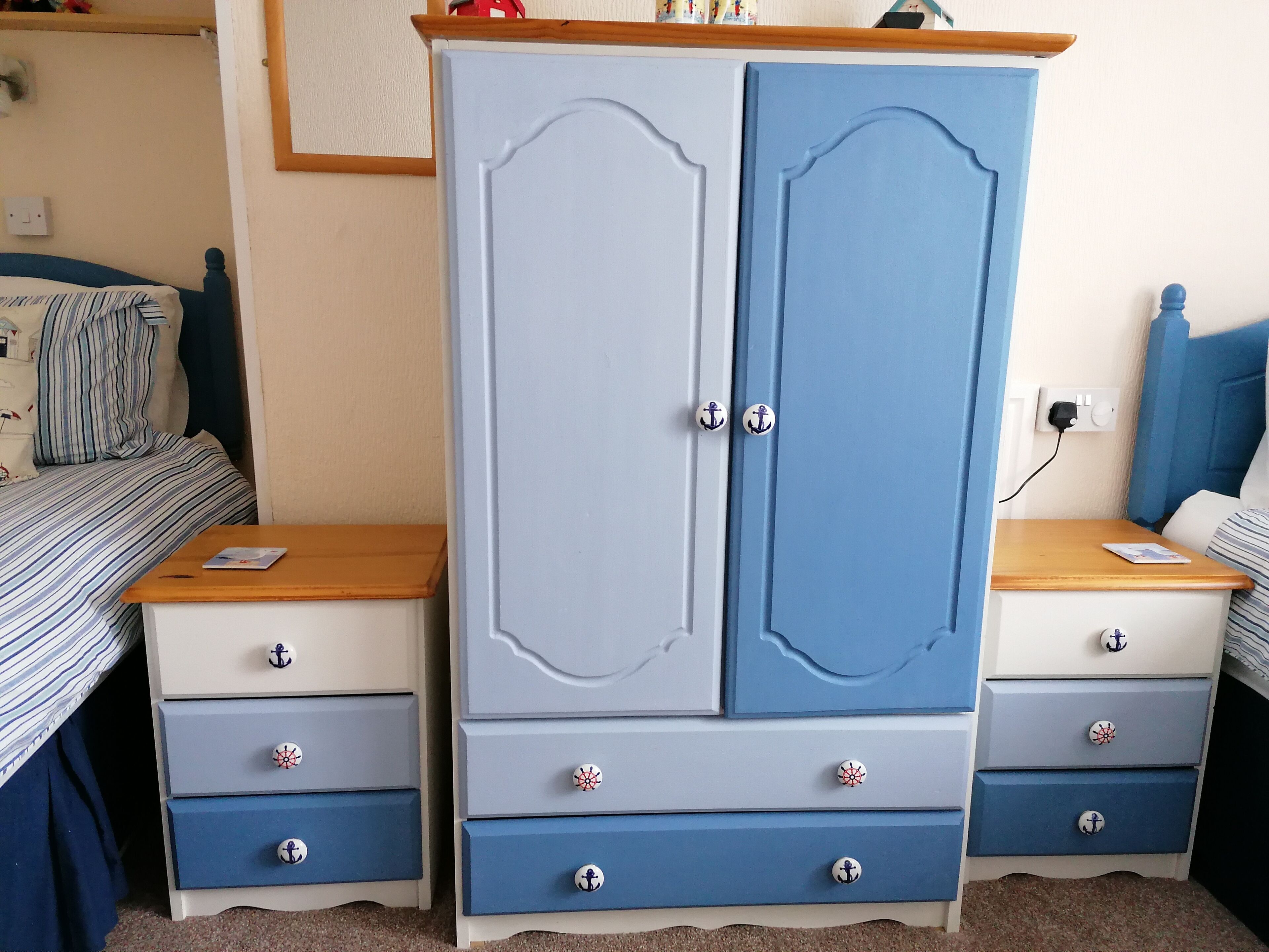 A bedroom with a large wardrobe, two bedside tables, a bed with striped bedding, and a nightstand with a lamp.