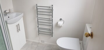 Un baño con un lavamanos blanco, un perchero, un inodoro y una puerta con pomo de latón.