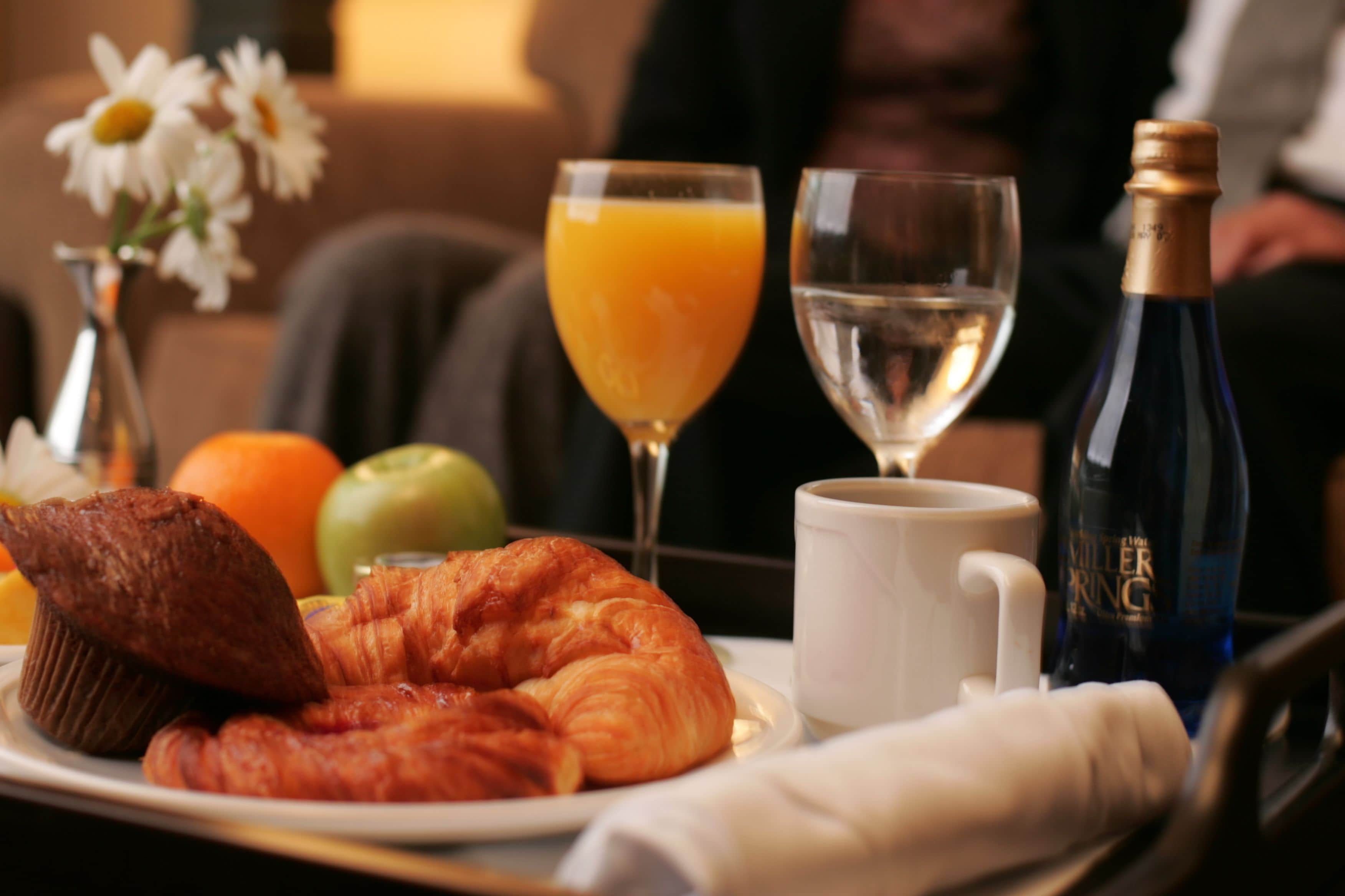 Bandeja de desayuno con cruasanes, un muffin, una naranja y un vaso de jugo de naranja.
