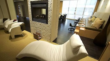 A hotel room with a massage chair, a small table with a bottle, and a view of the dining area.