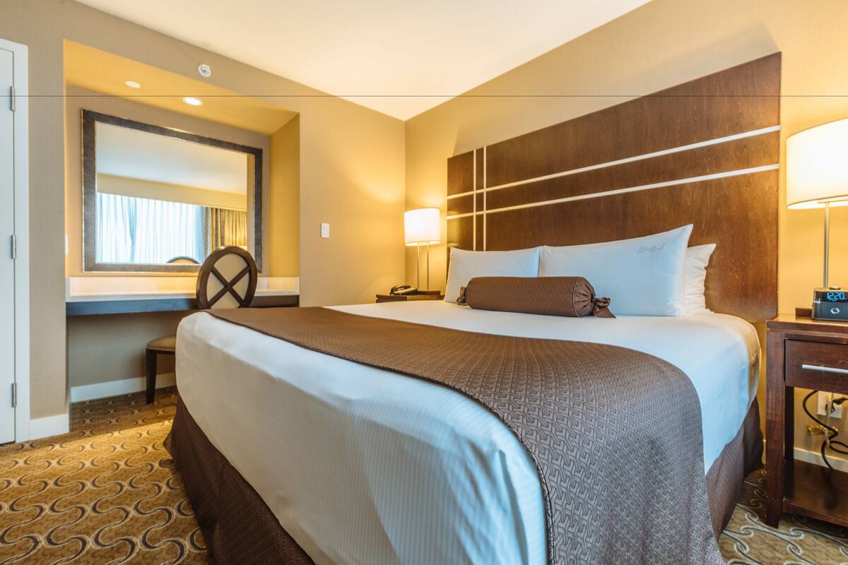 Een hotelkamer met een groot bed, een bureau, een stoel, een lamp en een nachtkastje.