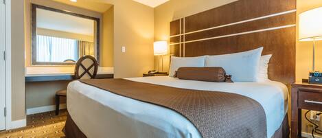 A hotel room with a large bed, a desk, a chair, a lamp, and a nightstand.