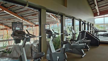 A gym with multiple exercise machines, a pool, and large windows offering views of the outdoors.