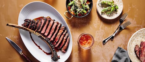 A steak with a side of asparagus and a glass of red wine on a table.