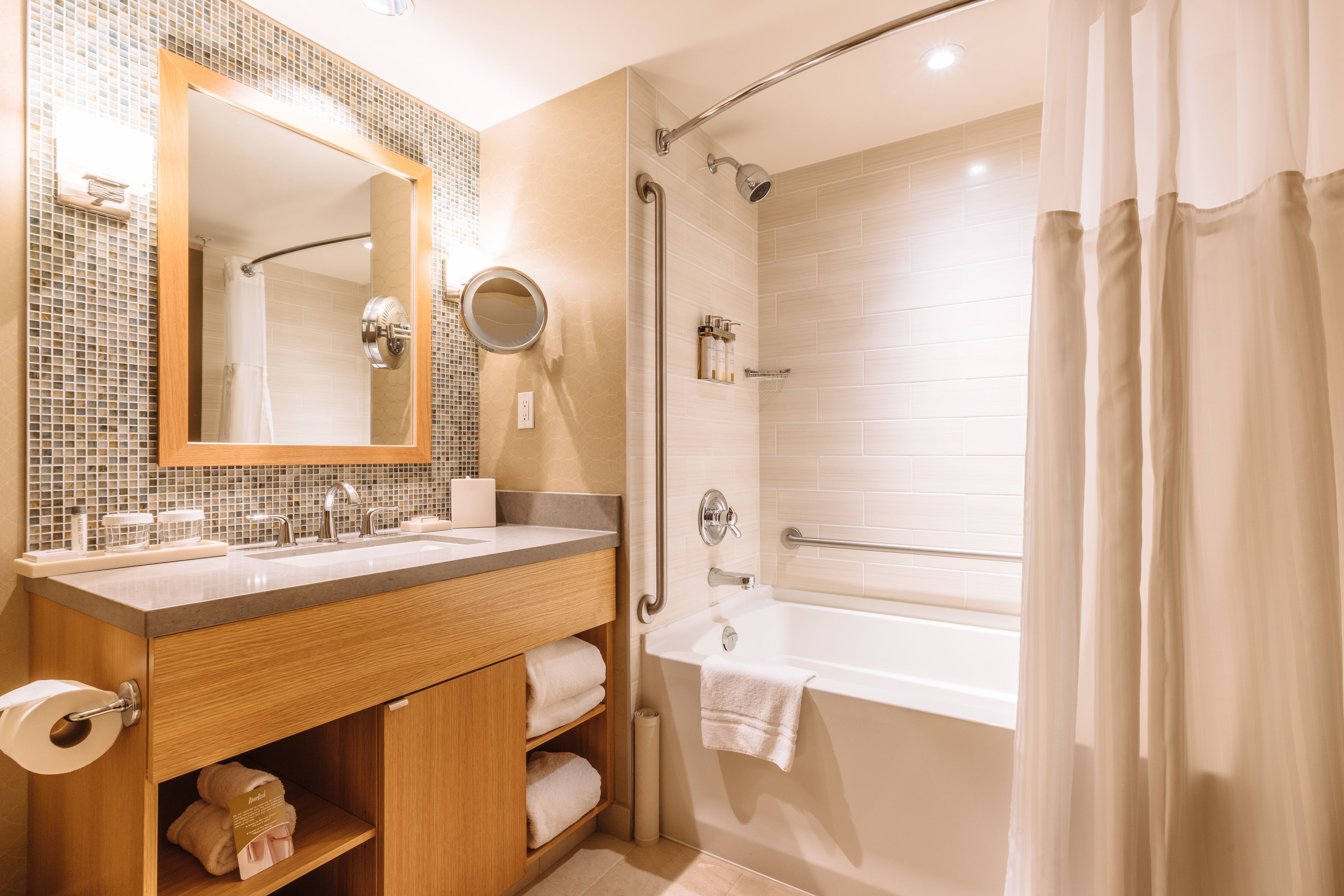 A modern bathroom with a wooden vanity, dual sinks, a large mirror, a bathtub, and a shower with a glass door.