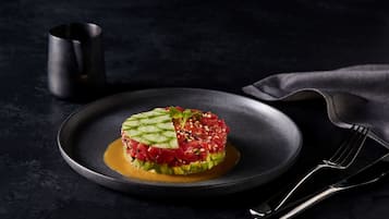 A dish of raw tuna tartare on a dark plate with a fork and a cup beside it.