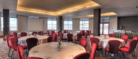 A conference room with multiple round tables, red chairs, and a carpeted floor.