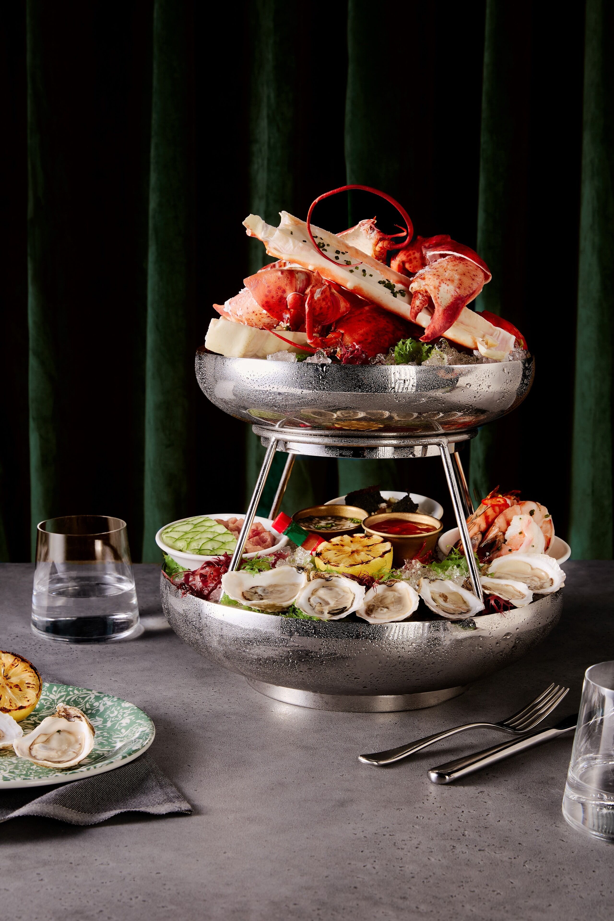 A seafood platter with various types of seafood and sides, including oysters and shrimp, on a metal stand.