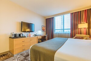 Habitación de hotel con cama, escritorio, televisor de pantalla plana, cafetera y lámpara.