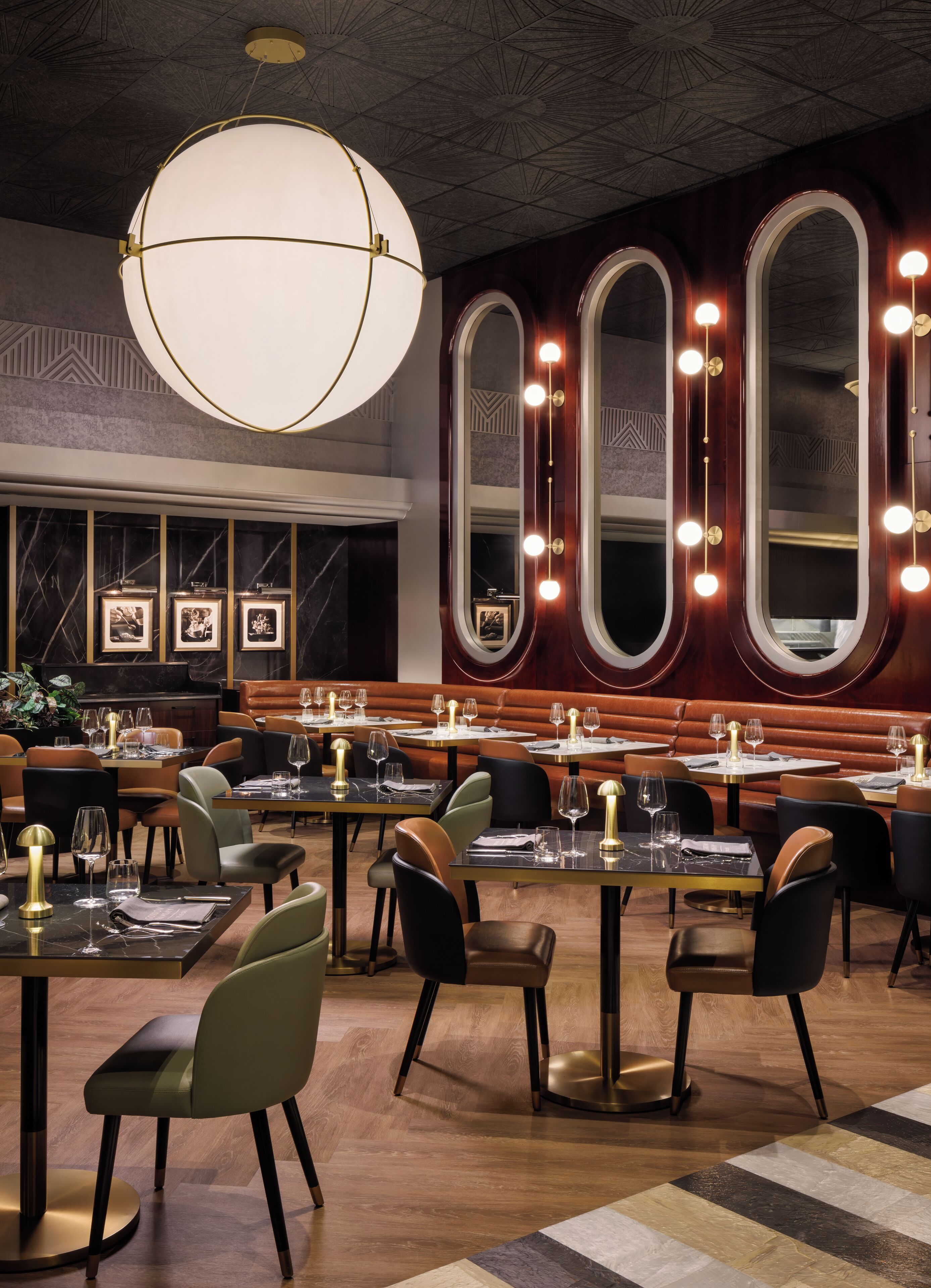 A restaurant interior with round tables, cushioned booths, and a large chandelier.