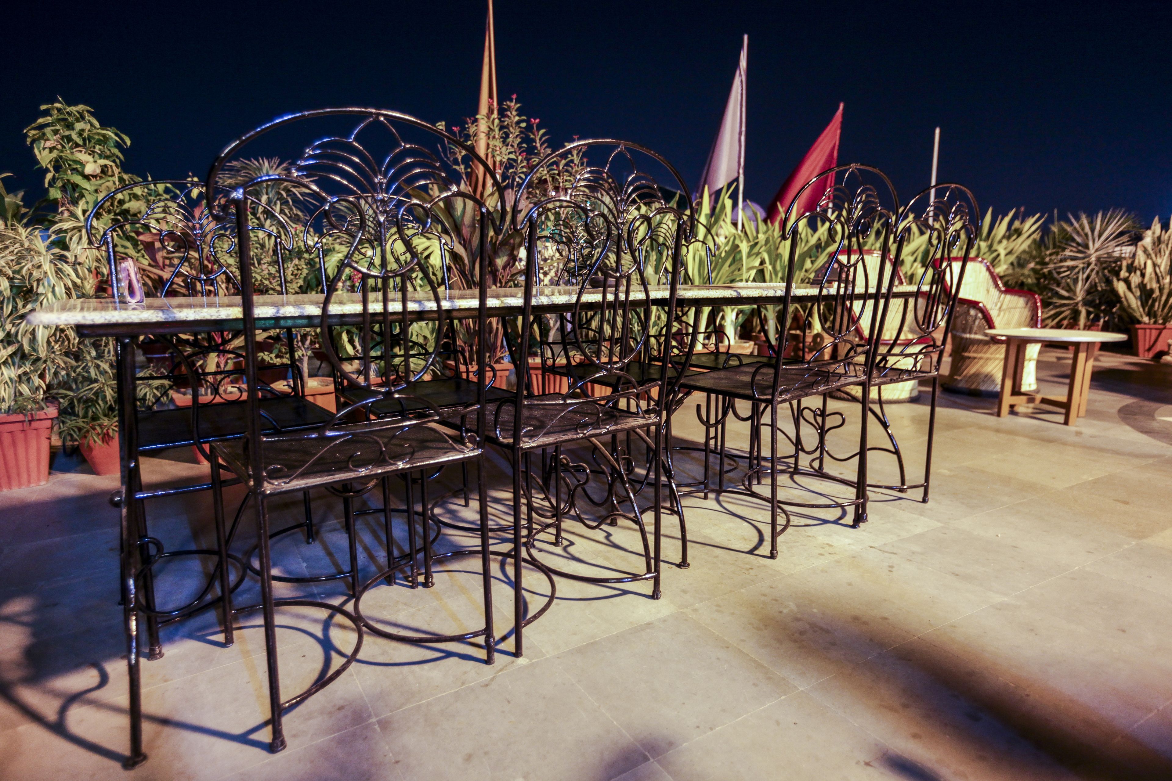 Een terras met een metalen tafel en stoelen, omringd door plantenpotten.