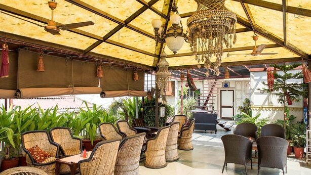 Een overdekt terras met rieten meubels, een kroonluchter en potplanten.