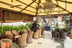 Uma área de estar coberta ao ar livre com móveis de vime, um candelabro e plantas em vasos.