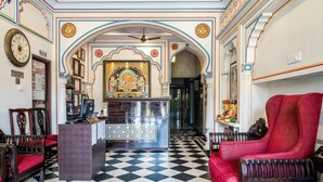 Een hotel lobby met een zwart-wit schakeerdvloer, een receptiebalie en rode bekleden stoelen.
