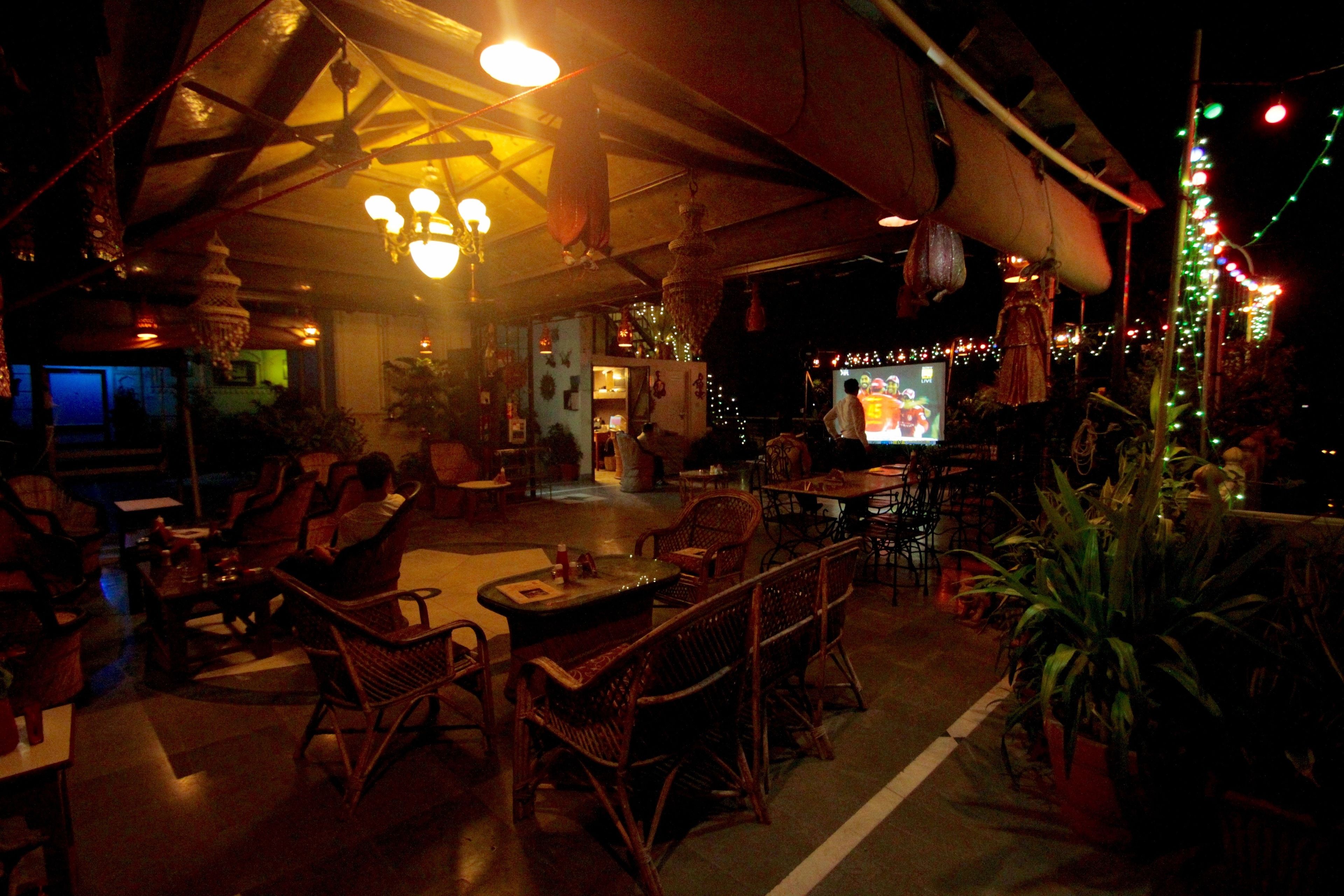Un espace de restauration intérieur aménagé avec des meubles en osier, des décorations suspendues et un écran de télévision.