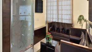 A modern living room with a glass partition, a sofa, a coffee table, and a TV mounted on the wall. - Hotel Marble Arch (New Delhi)