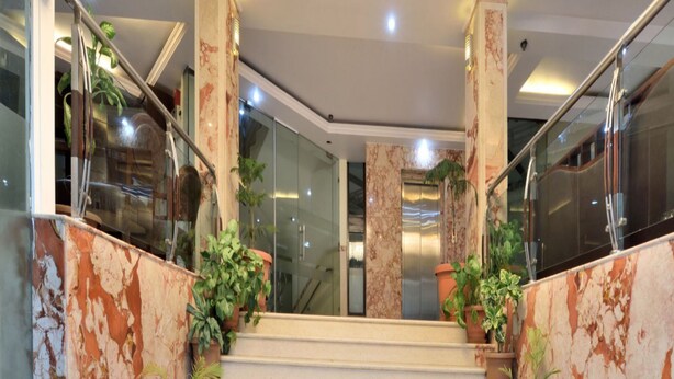 A grand staircase with marble columns, a modern chandelier, and potted plants. - Hotel Marble Arch (New Delhi)