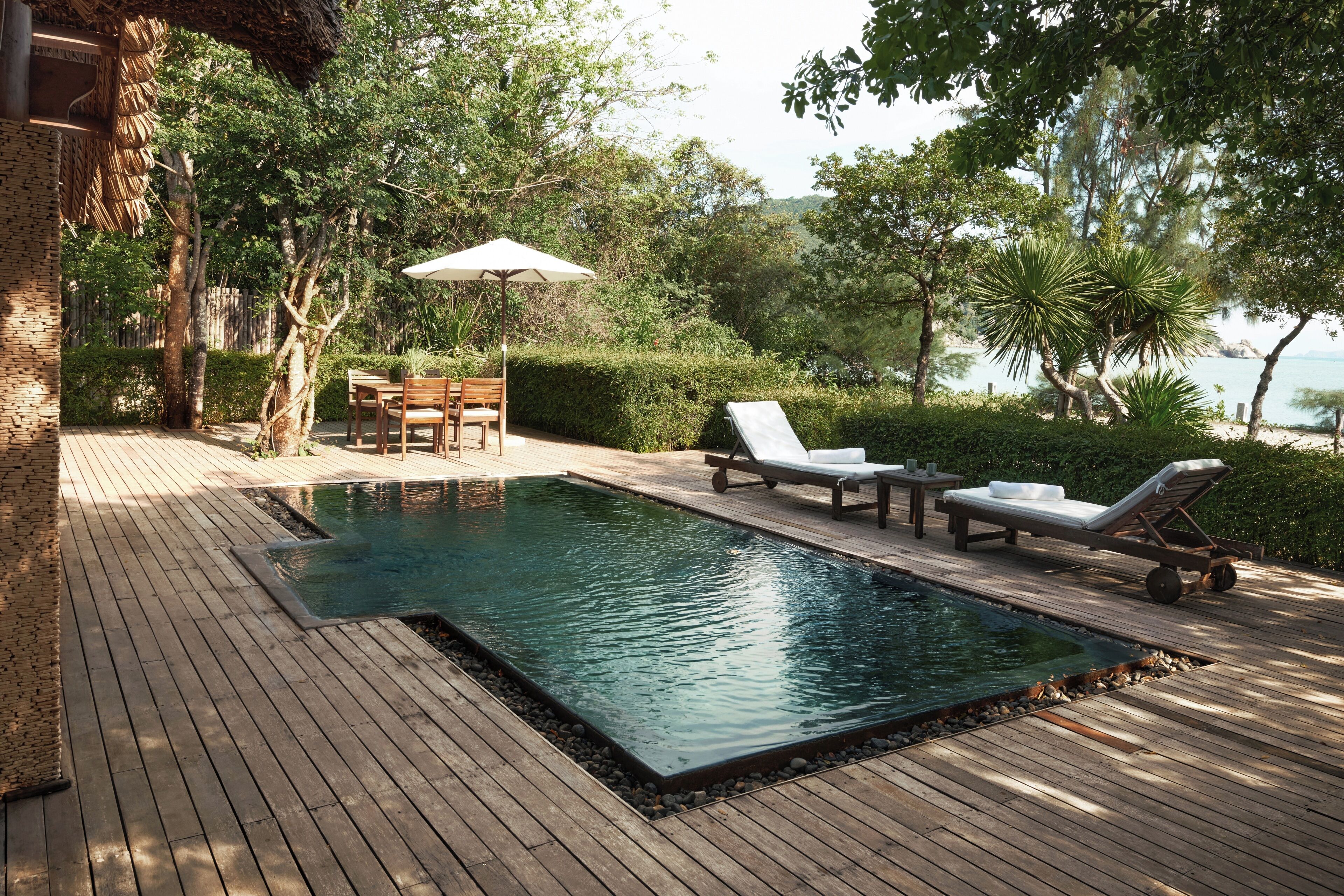 Une terrasse en bois avec une piscine, des chaises longues et une table avec des chaises.