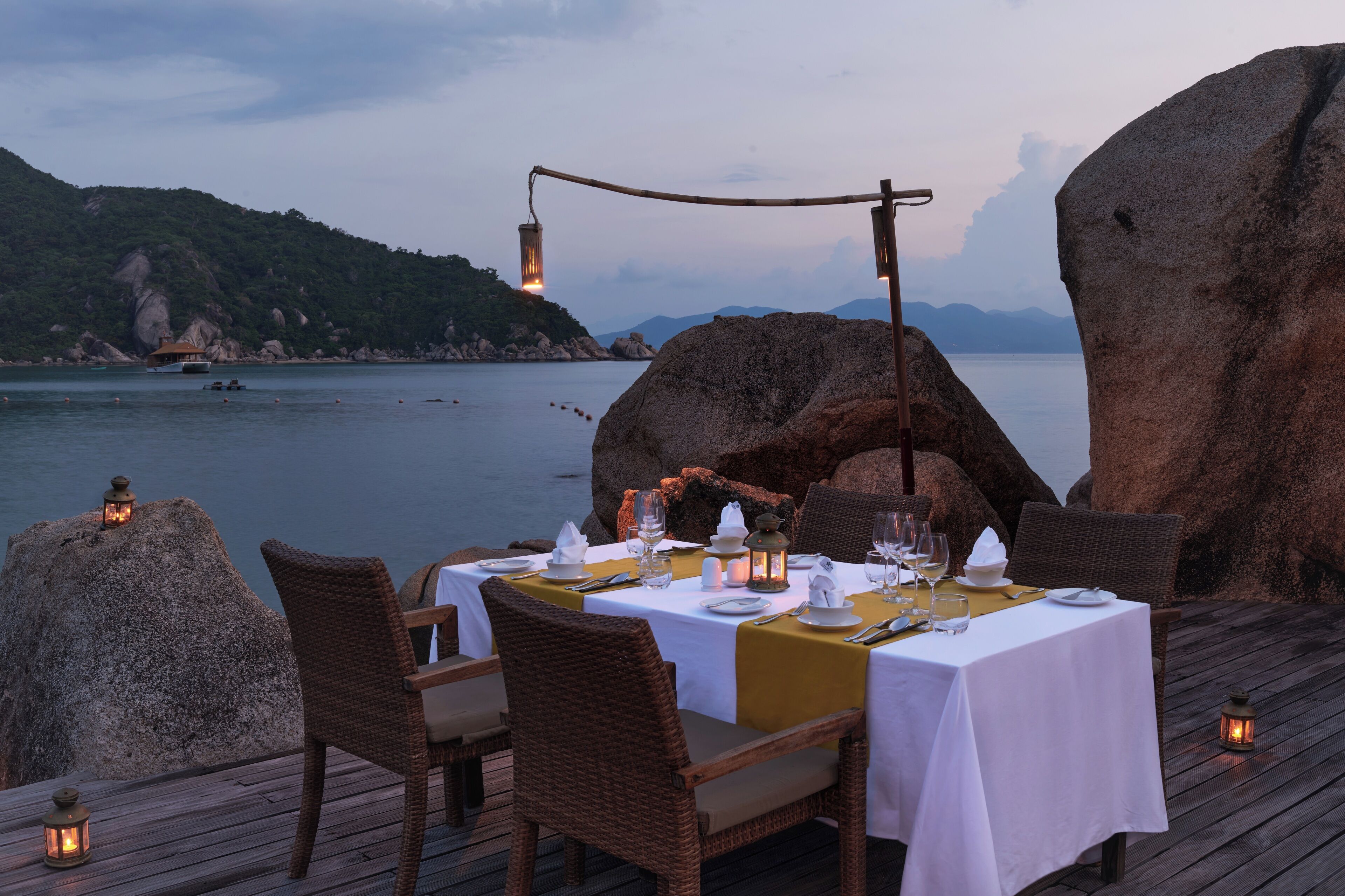 A dining table set for two with a view of the sea and mountains in the background.