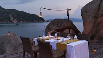 A dining table set for two with a view of the sea and mountains in the background.