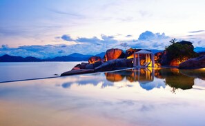 A tranquil lakeside scene with a gazebo and lounge chairs, surrounded by large rocks and mountains in the background. - L'Alya Ninh Van Bay (Dong Ninh Hoa)