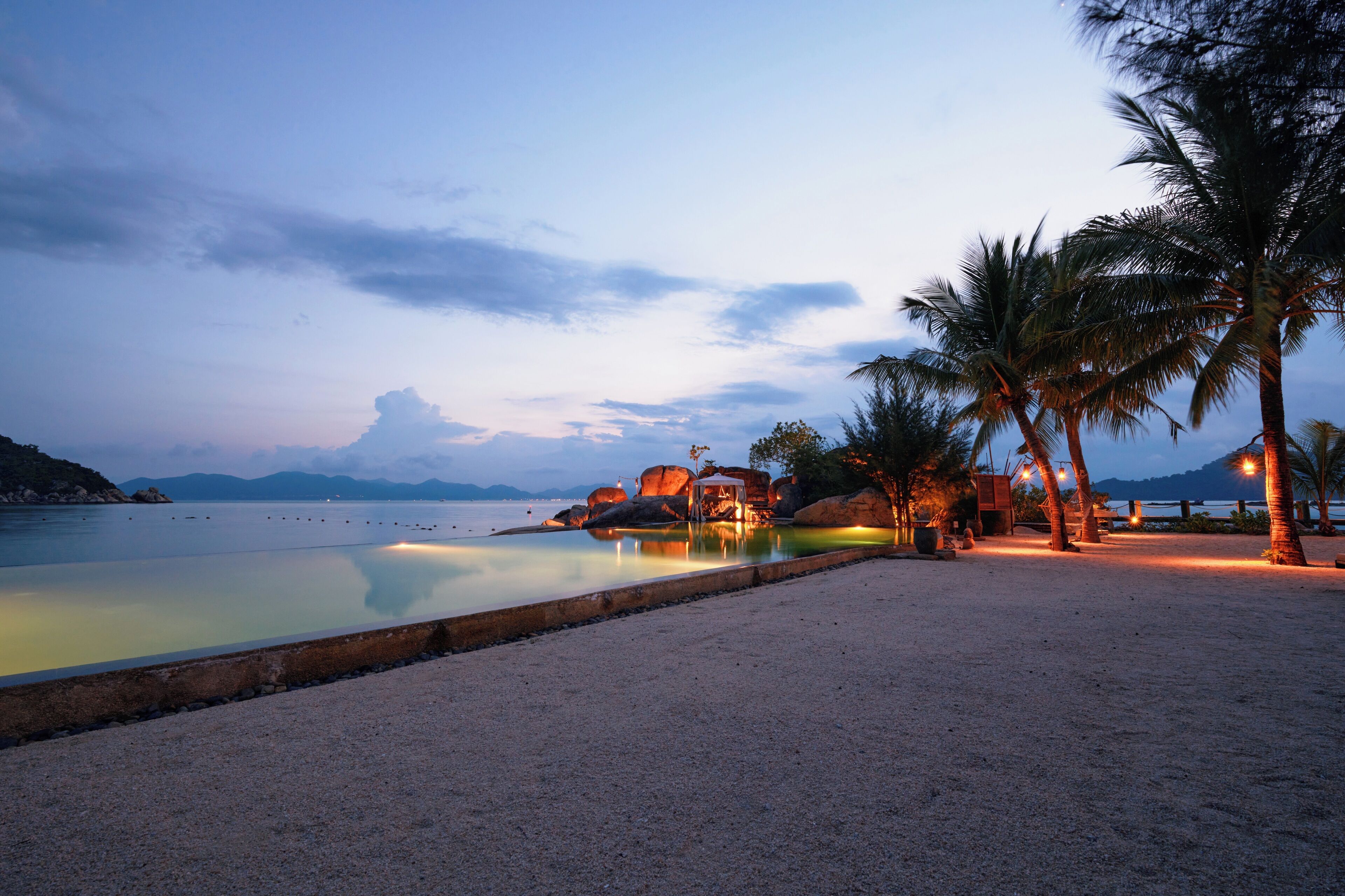 Ein Strand mit Pool, Palmen und Sonnenuntergang.