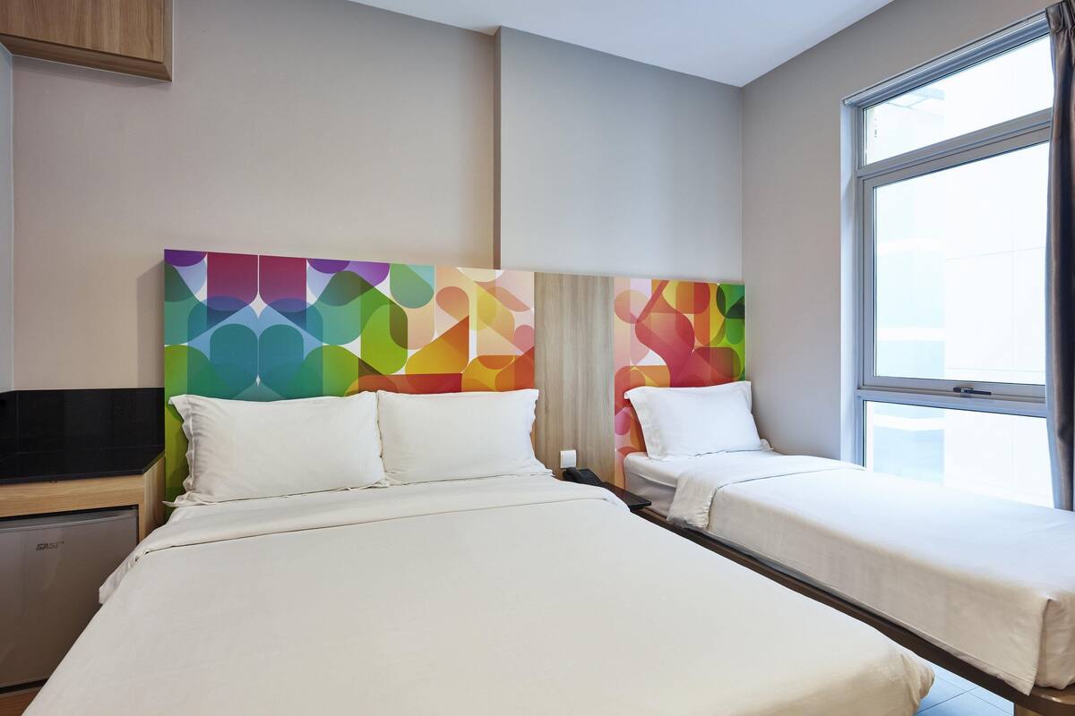 A hotel room with two beds, a TV, and a window with curtains.
