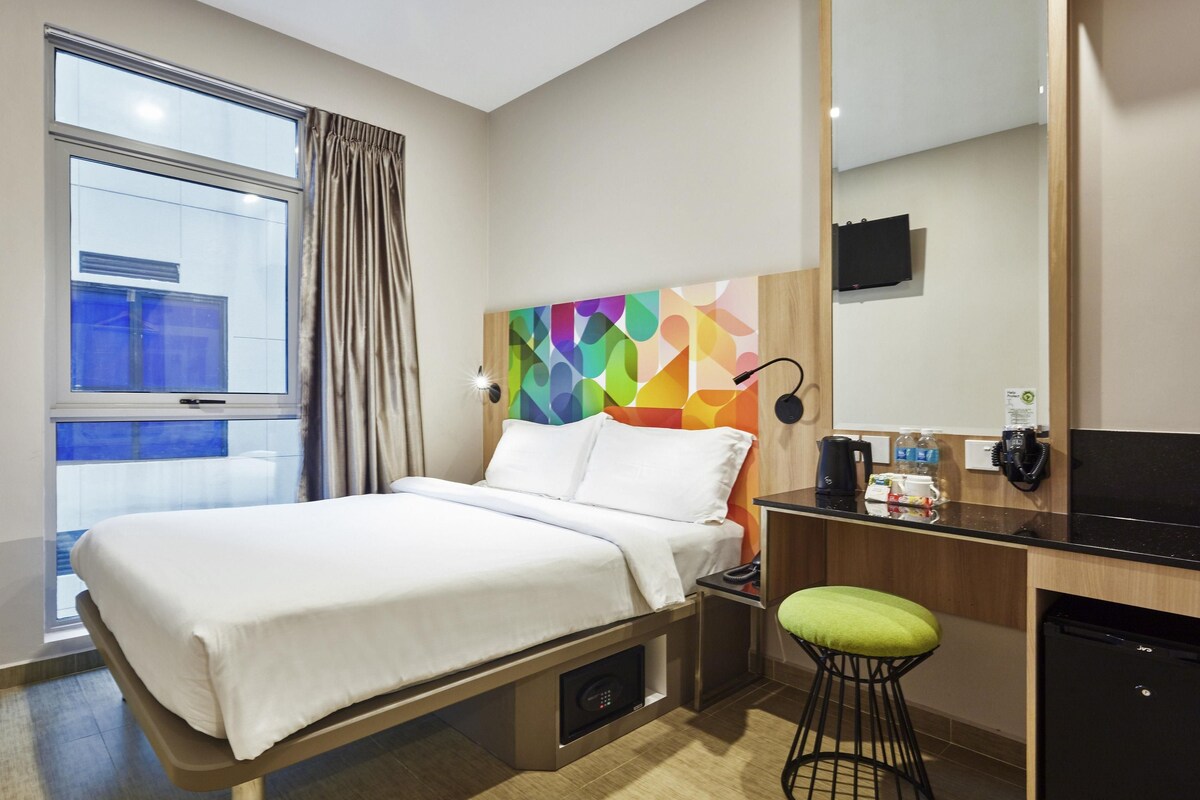 A hotel room with a bed, a desk, a chair, a coffee maker, and a TV.