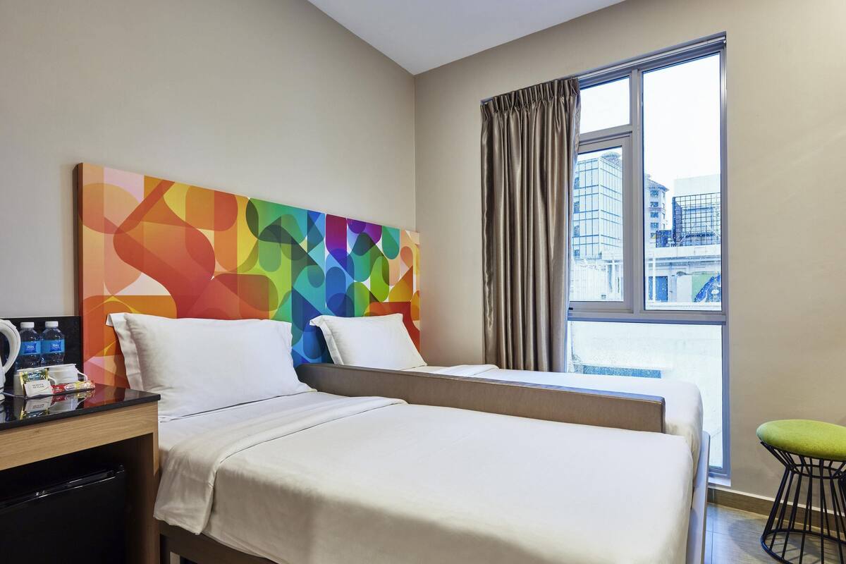A hotel room with a bed, a desk with a coffee maker, and a window with curtains.