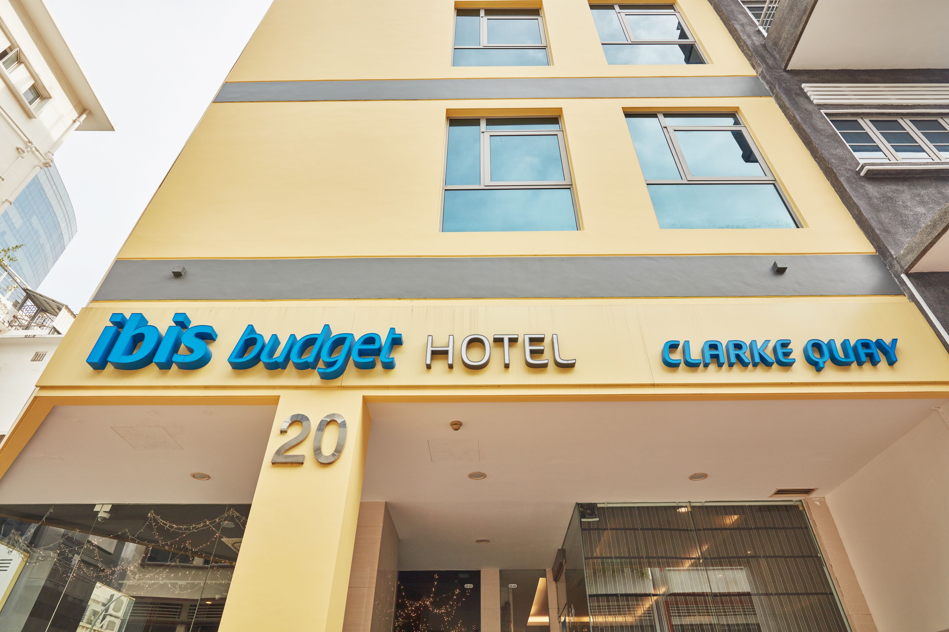 L’extérieur de l’hôtel ibis budget Clarke Quay se distingue par sa façade jaune, ses nombreuses fenêtres et le nom de l’hôtel, qui y est affiché en grand.