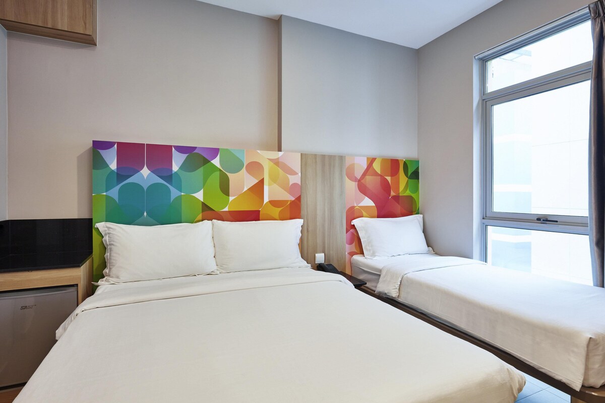 A hotel room with two beds, a TV, and a window with curtains.