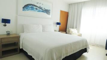A hotel room with a large bed, a bedside table, a nightstand, a chair, a desk, a lamp, and a painting on the wall.