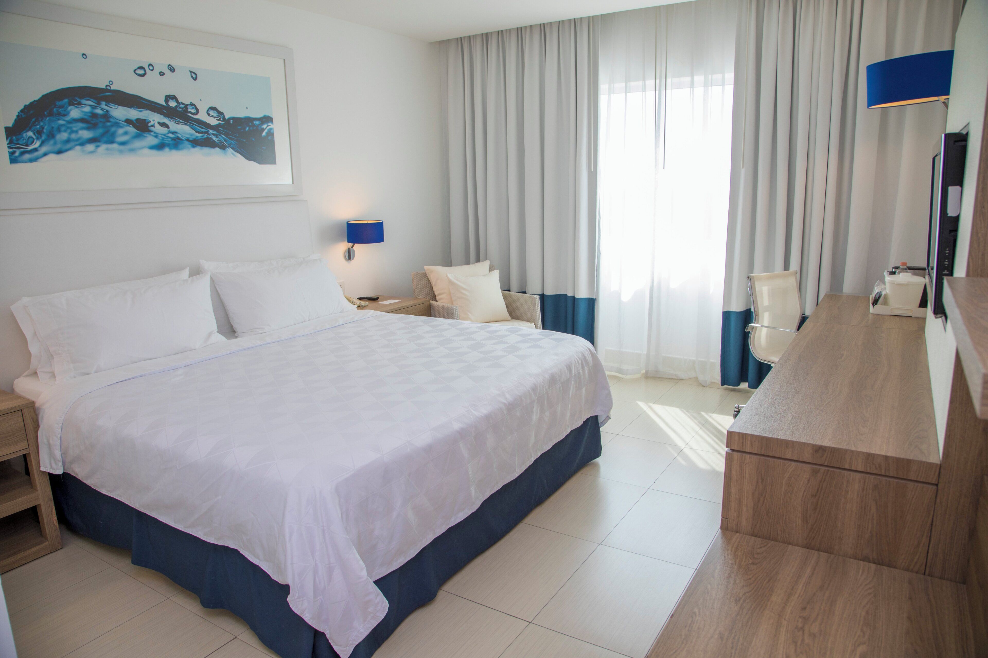 A hotel room with a large bed, a desk, a chair, a TV, and a bathroom.